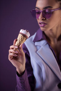 美丽的非洲裔美国女孩在时髦的紫外线太阳镜看冰淇淋在锥形, 孤立的紫色