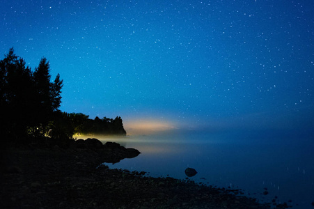 在湖岸边的星光夜。地平线上的水雾