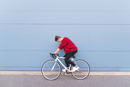 年轻人骑着一条白色的公路, 背景是蓝色的墙。时尚的时髦自行车骑自行车在城市周围
