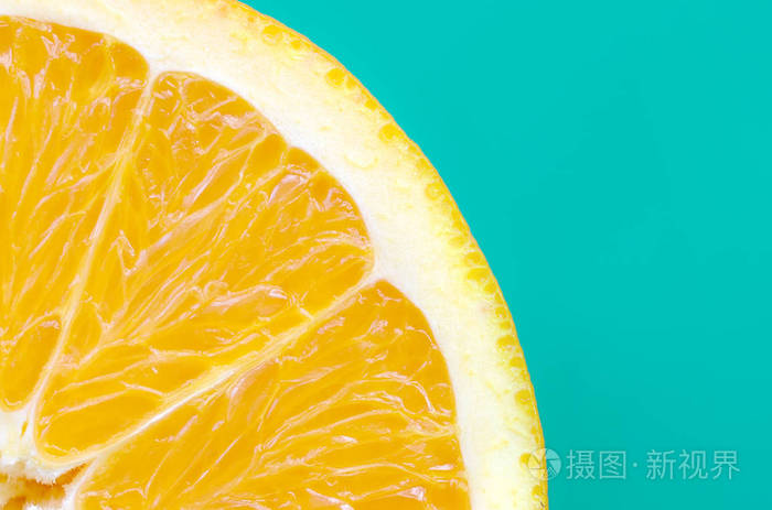 顶部的一个橙色的水果切片在明亮的背景绿松石绿色的颜色饱和柑橘纹理