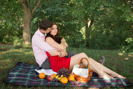 美丽的年轻夫妇在乡下野餐。幸福的家庭户外。微笑的男人和女人放松在公园里。关系