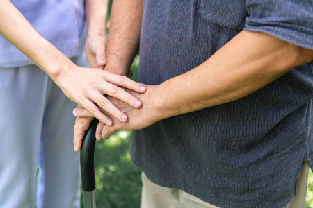 安慰的手。年轻的护士抱着老人的手在户外花园。高级护理护理人员和高级退休家庭服务概念。特写镜头
