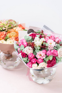 两个美丽的春天花束。在粉红色的桌子上的玻璃花瓶的各种颜色的花朵安排。明亮的房间, 白色的墙壁