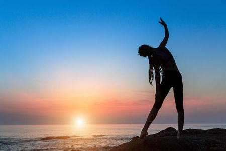 日落时分在海边做体操的年轻女子剪影