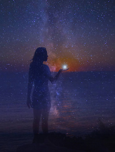 夜空中满是星星, 一只手上有颗星星的站立女孩的剪影.