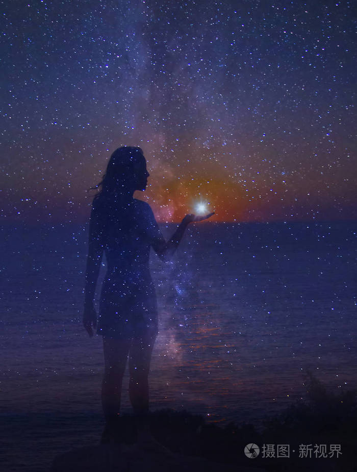 夜空中满是星星, 一只手上有颗星星的站立女孩的剪影.
