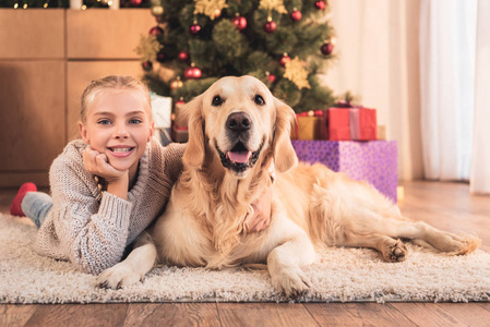 快乐的孩子和金猎犬狗躺在附近的圣诞树与礼物在家