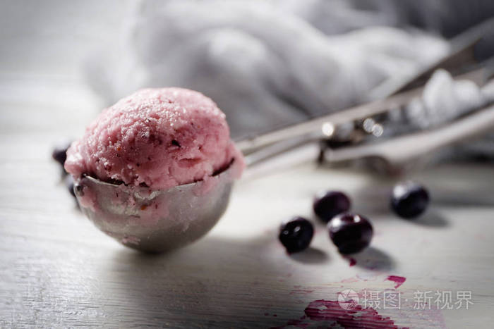 一勺蓝莓冰淇淋放在白色桌子上, 上面有几个浆果。侧面视图