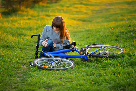 在日落的公园骑自行车骑车后, 膝盖关节疼痛的妇女。女孩坐下来与痛苦的表情。膝痛自行车伤