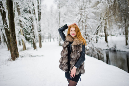 红头发的女孩穿着毛皮大衣在冬天下雪的公园散步