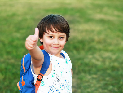 微笑的小男孩穿着背包显示在绿草背景 copyspace
