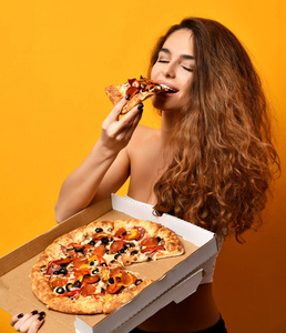 年轻美丽的妇女吃辣香肠比萨饼切片和举行整体比萨在箱子