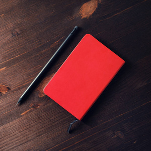 红色记事本和铅笔在深色木桌背景。平躺