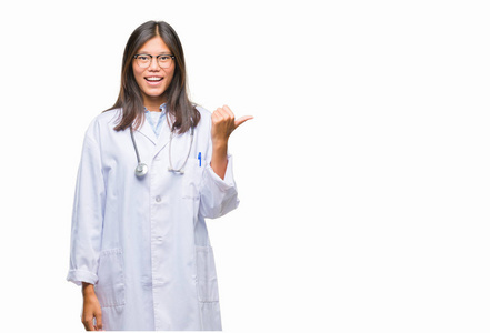 年轻的亚洲医生妇女在孤立的背景微笑着快乐的脸, 并指向侧面与拇指向上