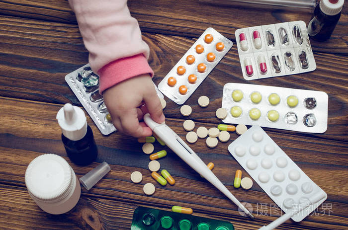 儿童的手在木桌上的药片上拿着温度计