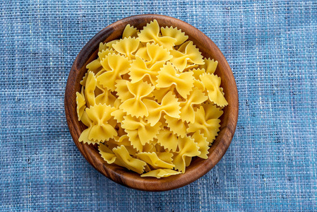 farfalle 通心粉面食在一个木碗在蓝色针织背景在中心。顶部特写