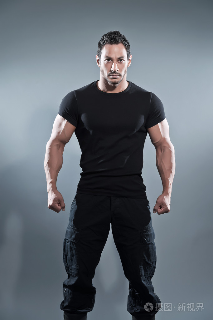 打击肌肉的健美男子穿着黑色的衬衫和裤子.工作室