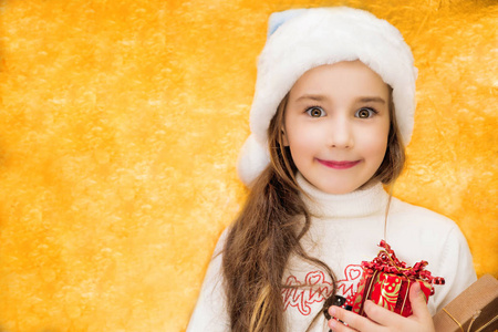 圣诞老人帽子的女孩在黄金背景与礼物在手