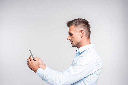 侧视图的英俊的成年男子使用智能手机查出的白色