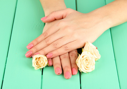 女人手中粉红色修指甲和鲜花的色彩木制背景