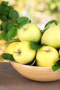 成熟的甜苹果有叶子在木碗中的自然背景