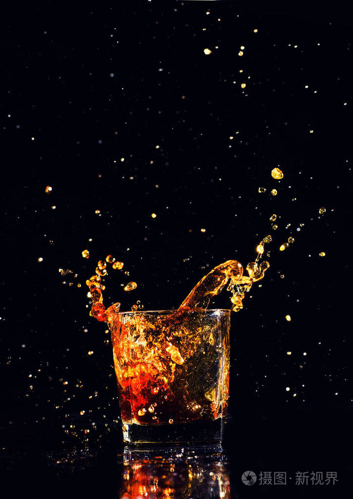 黑色背景飞溅的威士忌在玻璃杯白兰地的孤立拍摄
