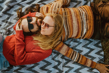 一个时髦的夫妇金发碧眼的女人和黑发人长发在毛衣冷和拥抱在毯子户外在日出