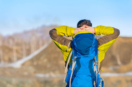 一个带着背包的年轻人紧握着他的双手在他的头后, 望向远方.照片
