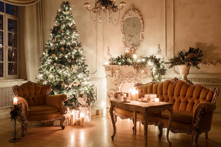 圣诞树, 花环, 蜡烛, 灯笼, 晚上的礼物。古典室内的白色房间与装饰壁炉, 沙发