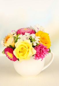 束美丽的鲜艳的花朵颜色杯里木桌上，轻的背景上