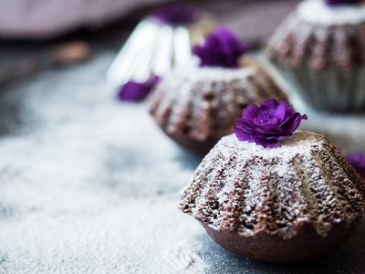 巧克力松饼用糖粉紫罗兰花选择性聚焦。黑暗