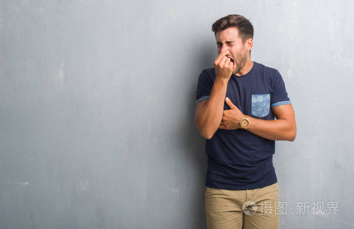 一个英俊的年轻人在灰色的垃圾墙上闻到了臭味和恶心难以忍受的气味用