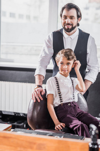 时尚的小孩子坐在椅子上的儿童理发店与理发师背景