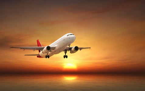 在日落时热带海洋上空飞行的飞机照片