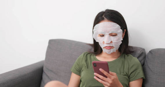 女性应用面部护肤面膜及在家使用手机