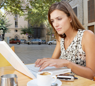 女商人在咖啡厅露台喝咖啡时使用一台便携式计算机
