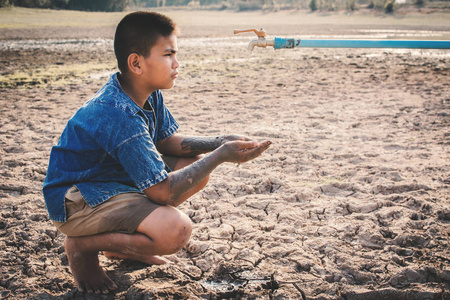 伤心的男孩想喝点水在裂缝地面上, 概念干旱和缺水危机照片