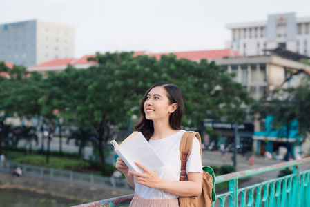 小美丽的女孩读书在桥梁与城市看法