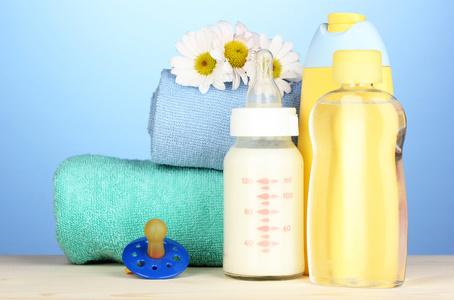婴儿奶瓶的牛奶 油和洗发水附近毛巾上的蓝色背景