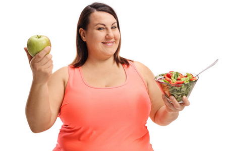 肥胖妇女拿着一个苹果和沙拉在白色背景隔绝了