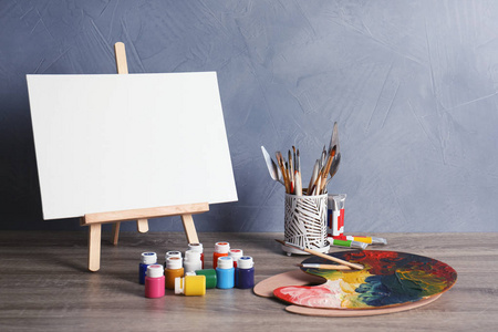 画架上的各种艺术家工具在桌子上反对彩色墙。文本空间