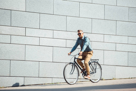 英俊时髦的人在太阳镜骑自行车在街道上