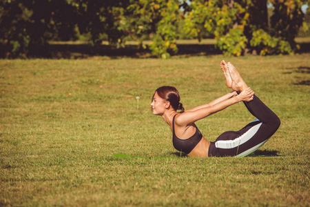 妇女在公园练习瑜伽, Dhanurasana 姿势