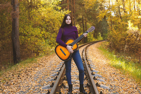 美丽的女孩与声学吉他在秋季公园。在铁路的青少年吉他