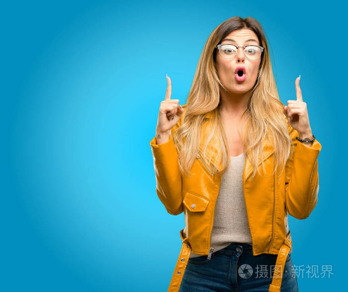 美丽的年轻女子高兴和惊喜欢呼表达哇姿态指向, 蓝色背景