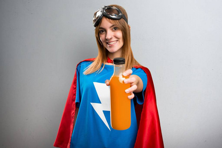美丽的超级英雄女孩拿着橙汁在灰色纹理背景