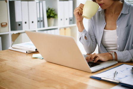 女性企业经营者的裁剪形象喝咖啡, 在笔记本电脑上工作