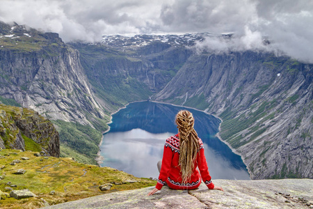 女孩坐在岩石和看挪威山风景。Trolltunga 岩石的踪迹。Ringedalsvatnet 湖, 挪威