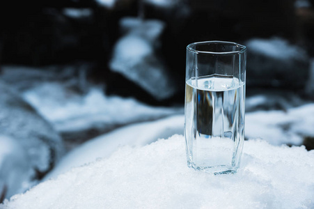 一个透明的玻璃杯, 饮用的在雪中矗立在冬日的一条清澈的寒山河的背景上