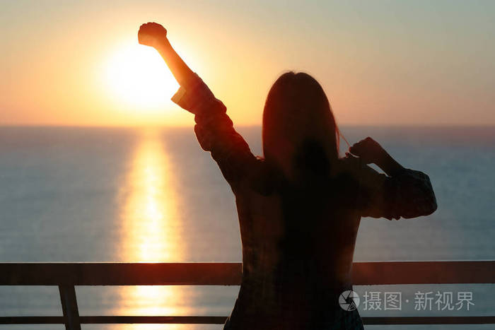 一个女孩的剪影在早晨日出光舒展胳膊醒来